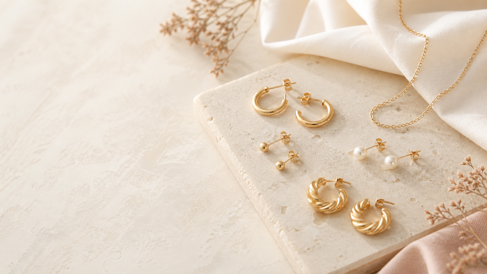 A selection of simple gold-tone hoops and stud earrings arranged on a neutral surface